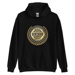 May include: Black hooded sweatshirt with a gold emblem that reads "WHEEL CERTIFIED ADDICT" in a circular design. The emblem is surrounded by a gold laurel wreath. The sweatshirt has a front pocket and a hood.