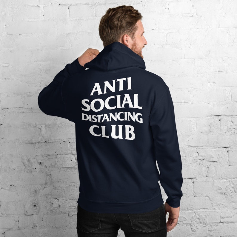 Peut inclure: Sweat-shirt &agrave; capuche bleu marine avec l'inscription blanche "ANTI SOCIAL DISTANCING CLUB" dans le dos. Le sweat-shirt a une capuche &agrave; cordon et des manches longues. La personne sur l'image porte le sweat-shirt.