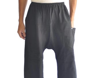 May include: Black harem pants with a wide leg design. The pants have an elastic waistband and pockets. The person in the image is also wearing a white tank top.