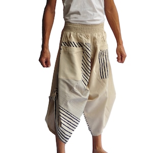 Könnte beinhalten: Eine Person trägt ein weißes Tanktop und eine beige Hose mit blau-weiß gestreiften Einsätzen. Die Hose hat eine lockere, fließende Passform und einen breiten Bund.