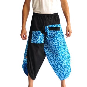 May include: Harem trousers in black and blue. The trousers have a black waistband with a drawstring and pockets. The lower section features a blue and white swirl pattern. The fabric is lightweight. The trousers are a loose fit.
