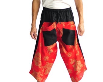 May include: Red and black patterned pants with a drawstring waist. The pants feature a dragon design in gold. The model is wearing a white tank top. The pants are loose-fitting and appear to be made of a lightweight fabric.