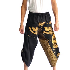 May include: Black and gold patterned pants with a drawstring waist. The pants feature a decorative design on the pockets and lower legs. The model is wearing a white tank top.