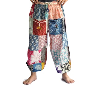 May include: Patchwork trousers featuring a variety of colourful fabric squares with diverse floral and geometric patterns. The trousers have an elastic waistband with a drawstring, two front pockets with tie closures, and elasticated ankle cuffs.