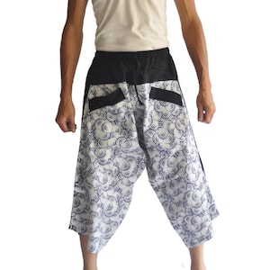 May include: Loose-fitting, cropped pants with a black waistband and pockets. The pants feature a white and blue circular pattern. The person in the image is wearing a cream-colored tank top.