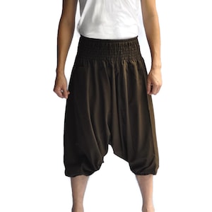 May include: A person wearing brown, loose-fitting pants with an elastic waistband and a white tank top.