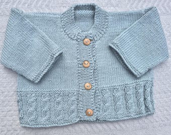 Peut inclure: Un cardigan de bébé tricoté bleu clair avec un col rond et des boutons en bois. L'ourlet inférieur présente un motif en tricot torsadé. Les manches sont de trois quarts.