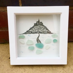 Puede incluir: Una ilustración enmarcada en blanco de un castillo en una colina con un camino que conduce a él. La ilustración está rodeada de vidrio de mar en tonos azules y verdes.