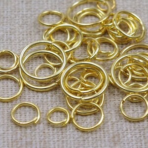Könnte beinhalten: Ein großer Haufen goldener Sprungringe in verschiedenen Größen. Die Ringe sind aus Metall und perfekt für die Schmuckherstellung oder das Basteln.