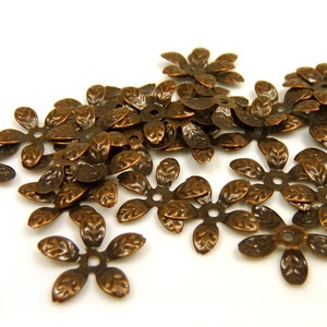Könnte beinhalten: Ein Haufen antiker kupferfarbener Metallblumenverzierungen mit einem fünfblattartigen Design. Jede Blume hat ein kleines Loch in der Mitte.