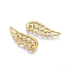 Könnte beinhalten: Zwei goldene Engelsflügel aus Metall mit einem dekorativen Design. Die Flügel sind ausgeschnitten und haben ein zartes, filigranes Muster.