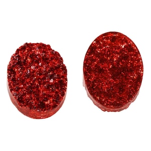 Könnte beinhalten: Zwei rote, glitzernde, ovale Cabochons. Die Cabochons sind flach und haben eine glitzernde, strukturierte Oberfläche.