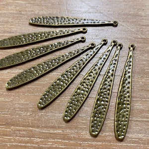 Peut inclure: Dix breloques en forme de feuille en métal doré antique avec une texture martelée et un anneau de saut en haut.