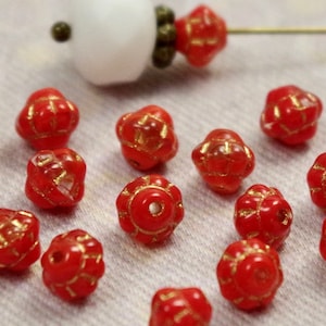 Könnte beinhalten: Eine Sammlung roter Glasperlen mit goldenen Akzenten. Die Perlen sind blumenförmig mit mehreren Spitzen.