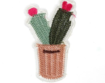 Könnte beinhalten: Eine gestickte Kaktuspflanze in einem Terrakotta-Topf mit rosa Blüten. Der Kaktus ist ein beliebtes Dekorationselement für zu Hause.