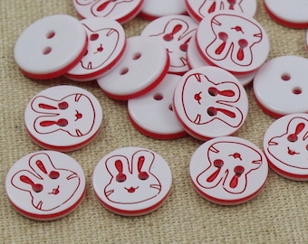 May include: A collection of white plastic buttons with red trim and a bunny rabbit design. The buttons have two holes.