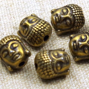 Könnte beinhalten: Sechs antike goldfarbene Buddha-Kopfperlen mit strukturierter Oberfläche. Die Perlen sind rund und haben ein Loch in der Mitte zum Aufziehen.
