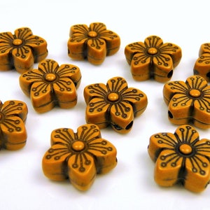May include: A collection of ten flower-shaped beads. Each bead is a warm, amber color with a detailed floral design in a darker brown. The beads have a hole for stringing, suitable for jewelry making or crafts.