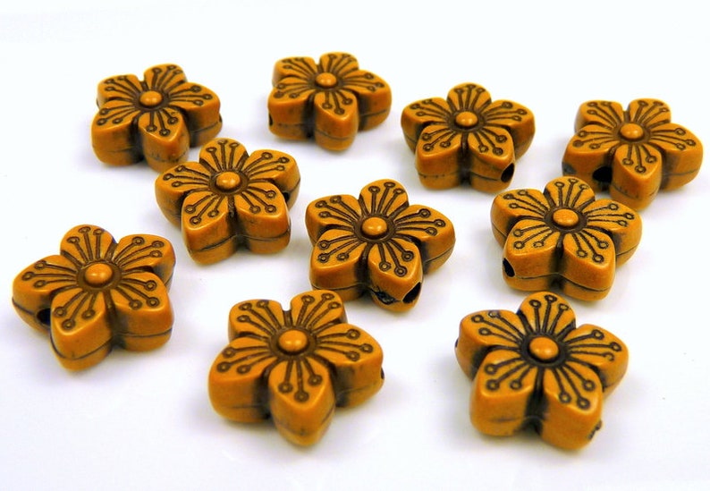 May include: A collection of ten flower-shaped beads. Each bead is a warm, amber color with a detailed floral design in a darker brown. The beads have a hole for stringing, suitable for jewelry making or crafts.