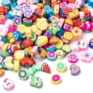 Könnte beinhalten: Eine große Auswahl an bunten Polymer Clay Perlen mit verschiedenen Frucht-, Tier- und Blumendesigns. Die Perlen sind perfekt für die Schmuckherstellung, Basteln und andere kreative Projekte.