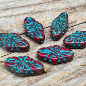 May include: Six red and turquoise glass beads with a decorative design. The beads are oval shaped and have a mottled appearance.