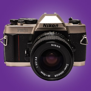 Appareil Photo Argentique Nikon FM10 + Objectif Zoom Nikkor 35-70mm - Pour Pièces, Dos Cassé, Vendu Tel Quel