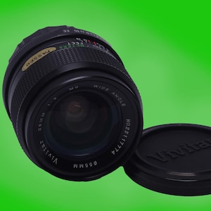 May include: A black Vivitar 28mm wide angle lens with a silver ring and the text "Vivitar 28mm 1:2.8 055MM NO.2211774 WIDE ANGLE" printed on the side.