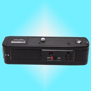 Puede incluir: Accesorio de cámara Minolta Auto Winder G negro con un interruptor de encendido/apagado rojo y una perilla negra. El texto "Minolta Auto Winder G Japan" está impreso en la parte delantera.