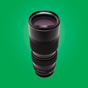 May include: A black camera lens with the text "NICA UC ZOOM-NICAR 62/8" printed on the side. The lens has a black rubber ring around the front and a silver ring around the back.