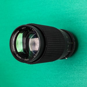 May include: A black camera lens with the text "AUTO ZOOM 80-200mm CPC OCT 1:4.0" printed on the side.