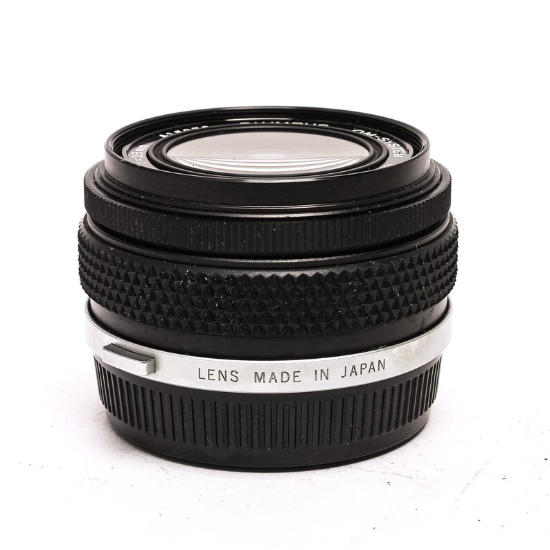 May include: A black camera lens with a silver band that reads "Lens Made in Japan".