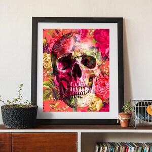 May include: A framed print featuring a skull with a floral pattern in shades of pink, red, and green. The skull is surrounded by flowers and leaves, creating a vibrant and colourful design.