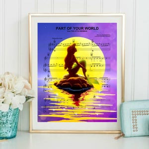 Könnte beinhalten: Ein gerahmter Druck mit Noten und einer Silhouette von Arielle aus Arielle, die Meerjungfrau. Das Kunstwerk zeigt eine leuchtend gelbe Sonne, einen lila und blauen Himmel und den Text "PART OF YOUR WORLD". Das Bild befindet sich in einem goldenen Rahmen.