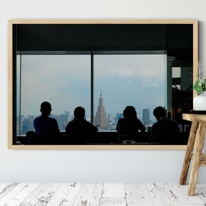 May include: A framed photograph of four people silhouetted against a city skyline, looking out a window. The city skyline includes a tall building with a radio antenna.