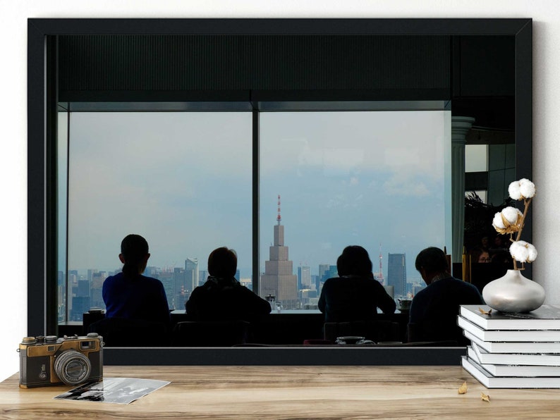 May include: Silhouettes of four people looking out a large window at a city skyline. The city is in the distance and the people are in the foreground. The window is framed by a black frame.