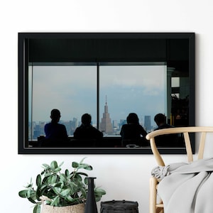 May include: A framed photograph of a city skyline viewed from a window. Four people are silhouetted in the foreground, looking out at the cityscape. The building in the center of the skyline has a red antenna.