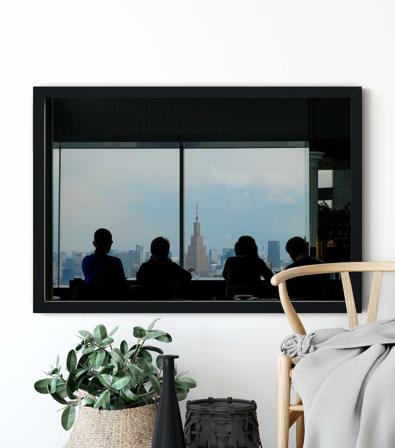 May include: A framed photograph of a city skyline viewed from a window. Four people are silhouetted in the foreground, looking out at the cityscape. The building in the center of the skyline has a red antenna.