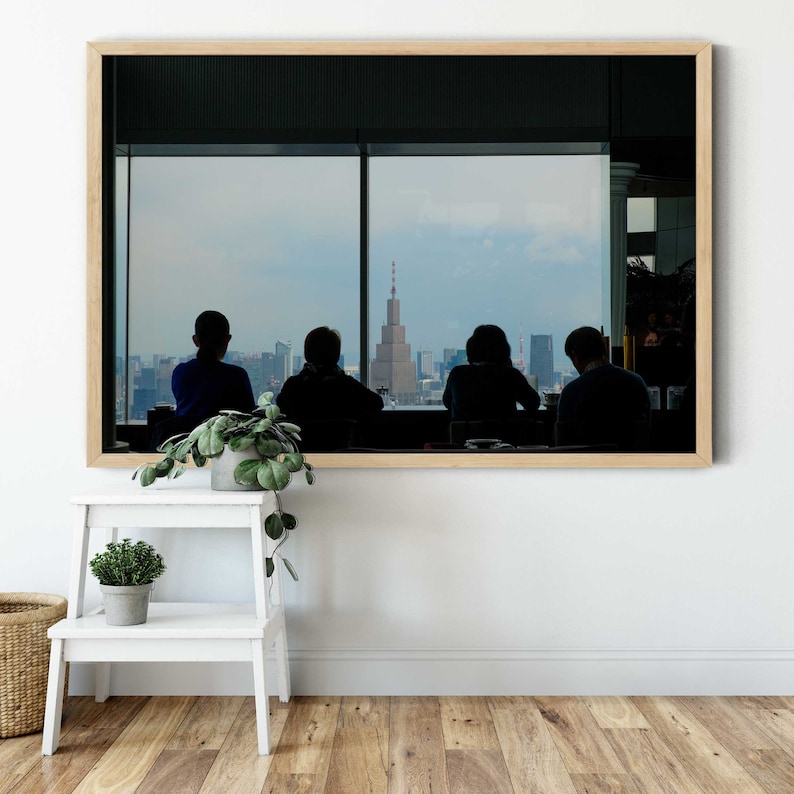 May include: A framed photograph of four people sitting in front of a large window with a view of a city skyline. The people are silhouetted against the window, and the city skyline is visible in the background.