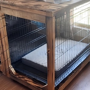 Pode incluir: Uma gaiola de madeira para cães com frente e laterais em malha de arame. A gaiola tem uma estrutura de madeira tingida escura e uma bandeja de metal na parte inferior. No interior, há uma cama para cães de cor clara. A gaiola foi projetada para o conforto e segurança dos animais de estimação.