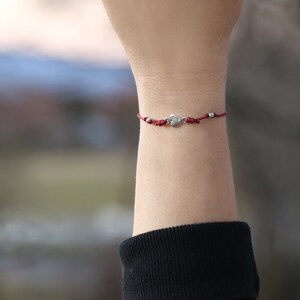 May include: A red string bracelet with a silver heart charm and silver beads.