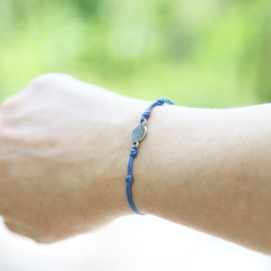 Puede incluir: Un brazalete de cordón azul con un dije plateado con diseño de brújula.