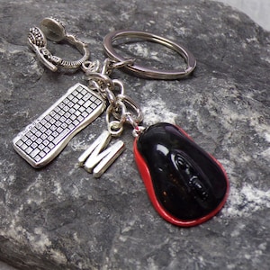 Könnte beinhalten: Ein silberner Schlüsselanhänger mit einer Computer-Tastatur, einer schwarzen und roten Computermaus und einem silbernen Anhänger mit dem Buchstaben 'M'. Der Schlüsselanhänger ist an einem silbernen Schlüsselring befestigt.