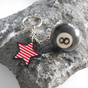 Könnte beinhalten: Ein silberner Schlüsselanhänger mit einem rot-weiß gestreiften Stern-Anhänger und einem schwarzen 8-Ball-Anhänger.