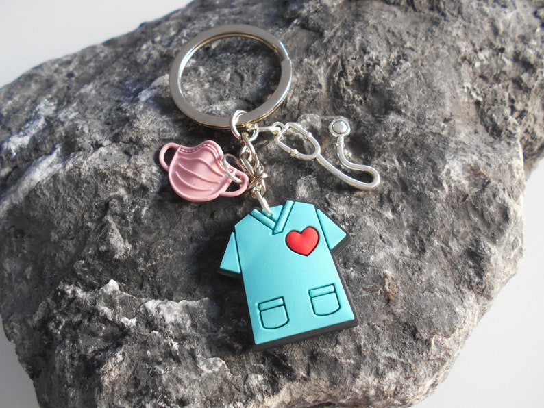 May include: A blue scrubs keychain with a red heart, a pink face mask, and a silver stethoscope charm.