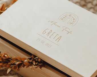 May include: A wooden keepsake box with a light wood finish and a white lid. The lid has a rainbow design and the text "Welcome to the world Greta 21.04.2023".