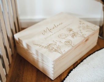 May include: A rectangular light-colored wooden storage box with a hinged lid. The top surface features a laser-engraved floral design and the name Marlene in script, along with the German text Die Welt ist voller Wunder. Die Welt ist voller Wunder.