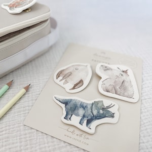 Könnte beinhalten: Ein Set mit vier Aquarell-Tieraufklebern auf einer beigefarbenen Karte. Die Aufkleber zeigen einen Dinosaurier, einen Pinguin, einen Bären und einen Vogel. Die Karte trägt den Text "handle with love" und eine Website-Adresse.