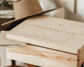May include: A wooden box with the words "memories" and "Jacqueline & Benedikt" engraved on the lid. The box is sitting on a wooden table with a small bouquet of flowers and a pair of earrings.