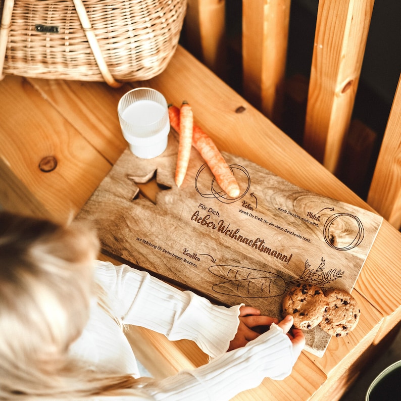 May include: A wooden serving board with a star design and the text "F&uuml;r Dich, lieber Weihnachtsmann!"  The board also has illustrations of carrots, cookies, and milk.