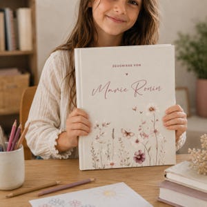 Könnte beinhalten: Ein hellbeiges Hardcover-Buch mit dem Text "ZEUGNISSE VON" über dem Namen "Marie Ronin" in Schreibschrift. Der Einband ist mit einer zarten Illustration von Wildblumen, Stängeln und Schmetterlingen in sanften Rosa- und Brauntönen verziert.